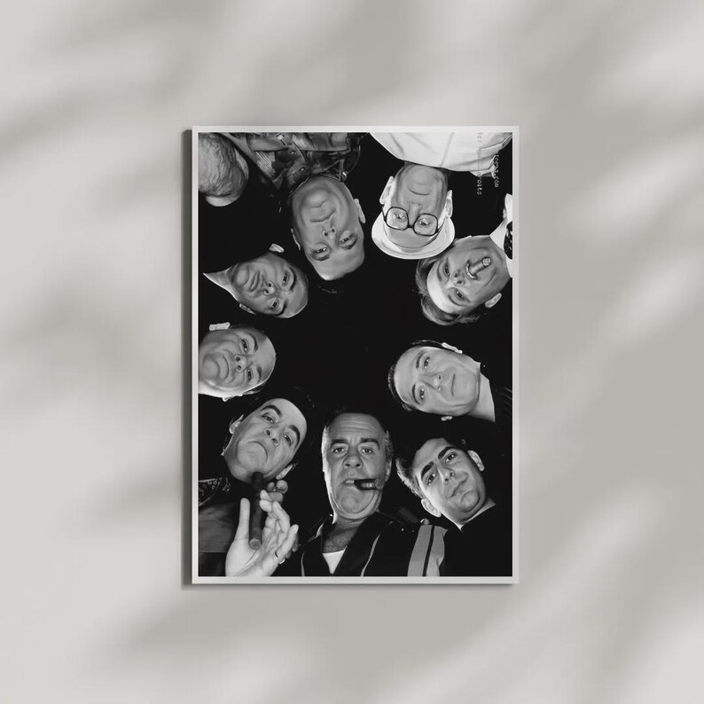 May include: A black and white photographic print featuring a low-angle, circular composition of several individuals looking downward. The subjects are arranged in a ring, with some wearing hats and glasses, and one individual holding a cigar.