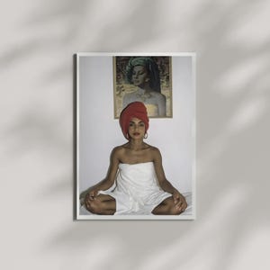 May include: A framed wall art print featuring a person sitting in a cross-legged position, wrapped in a white towel with a matching red head wrap. Above the person, a second framed portrait depicts a figure with a green head wrap and gold accents.