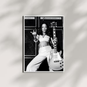 May include: A black and white photograph of a person with long dark hair wearing a cropped long-sleeve top and high-waisted trousers, holding an electric guitar. The person is positioned in front of a stack of large rectangular speaker cabinets.
