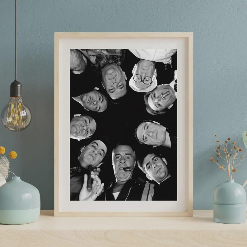 May include: A black and white framed print featuring a low-angle, circular composition of several men looking downward. The individuals are captured in a group, with some wearing glasses and one holding a cigar, set against a dark background.