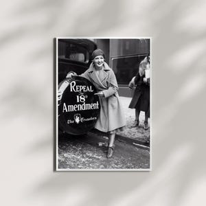 May include: A black and white photograph showing a person in a long coat leaning against a vehicle spare tire cover. The cover features the text Repeal The 18th Amendment and The Crusaders. Another person stands in the background wearing a dark coat.