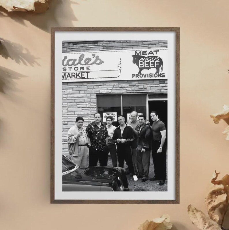 May include: A black and white framed print depicting a group of six men standing in front of a brick storefront labeled 'Meat Angus Beef Provisions'. The men are dressed in casual attire, and the front of a dark car is visible in the foreground.