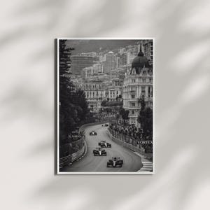 May include: A black and white vertical wall art print depicting a Formula One race on a winding city street circuit. Several race cars are driving in a line past grandstands and urban architecture. The word VORTEX is visible on trackside barriers.