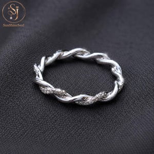 Op de afbeelding: Een zilverkleurige ring met een gedraaid touwontwerp. De band bestaat uit twee in elkaar gevlochten strengen, waarvan één met een gladde gepolijste afwerking en de andere bezet met kleine, heldere, fonkelende steentjes.