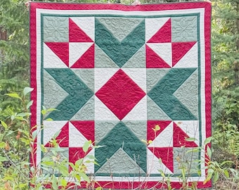 May include: A square quilt featuring a central red diamond surrounded by a geometric star pattern in shades of dark green, sage green, and white. The fabric displays intricate swirling and floral quilted textures with a solid red border.