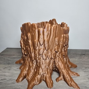 May include: A copper-colored, 3D-printed planter shaped like a tree stump. The object features a textured, rugged exterior mimicking natural bark with deep vertical grooves and ridges, and a hollow, open top for holding items or plants.