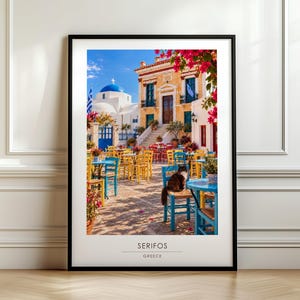 Op de afbeelding: Een ingelijste kunstdruk van een zonnig terras in Serifos, Griekenland. De afbeelding toont gele en blauwe stoelen en tafels, een kat op een stoel, felroze bougainvillea en een gebouw met een blauwe koepel onder een heldere blauwe lucht.