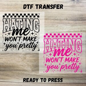 May include: Two DTF transfer designs with the text "Hating me won't make you pretty." One design is black and white, the other is pink. Both have a checkered border and star accents. The words "DTF TRANSFER" and "READY TO PRESS" are also visible.