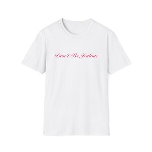 Peut inclure: T-shirt blanc avec l'inscription "Don't Be Jealous" en rose en cursive sur la poitrine. Le t-shirt a un col rond et des manches courtes. Le texte est centr&eacute; sur le devant du v&ecirc;tement.
