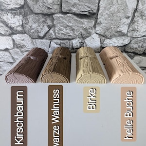 May include: Four semi-cylindrical log-shaped objects with textured bark surfaces, arranged in a row. Each piece features a small rectangular cutout on top. The colors range from dark brown to light beige, labeled Kirschbaum, schwarze Walnuss, Birke, and helle Buche.