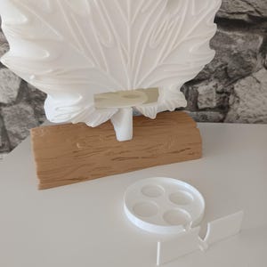 May include: A white 3D-printed maple leaf sculpture mounted on a textured tan log-shaped base. A separate white circular tray with four small indentations and a rectangular connector piece are positioned in front of the main leaf structure.