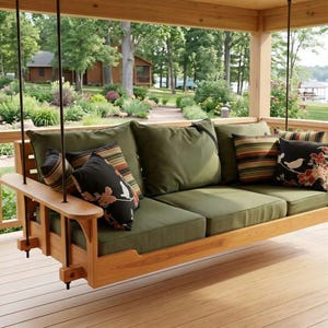 Op de afbeelding: Een houten verandaschommel met een natuurlijke lichtbruine afwerking, opgehangen aan zwarte touwen. De schommel is voorzien van drie olijfgroene zitkussens en diverse decoratieve kussens met zwarte, olijfgroene, gestreepte en bloemmotieven.