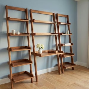 May include: Wooden ladder-style shelving units with multiple shelves and a desk area. The shelves are a warm brown color and are arranged against a light blue wall. Decorative items are placed on the shelves.