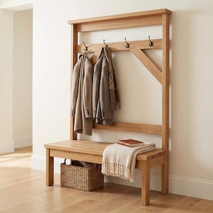 Könnte beinhalten: Eine Garderobenbank aus hellbraunem Holz mit einer Sitzfläche, einer Rückwand mit vier schwarzen Metallhaken und einer unteren Ablage. Ein geflochtener Korb steht unter der Bank, während eine beige Decke und ein Buch auf der Sitzfläche liegen.