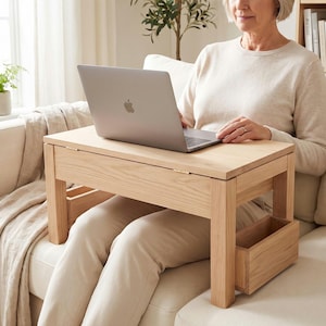 May include: A light-toned wooden lap desk featuring a rectangular flat top surface, four sturdy legs, and two side-mounted storage compartments. The desk is designed to sit over the lap, providing a stable platform for a laptop computer.