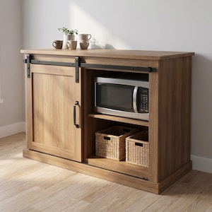 Puede incluir: Un mueble de almacenamiento de madera marrón con una puerta corredera que tiene un tirador y un riel de metal negro. La sección abierta contiene un microondas plateado en el estante superior y dos cestas de mimbre en el estante inferior.
