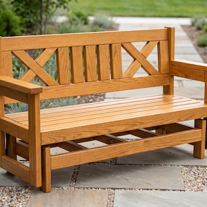 May include: A light brown wooden bench featuring a slatted seat and a backrest with two X-shaped patterns flanking three vertical slats. The bench has flat armrests and a sturdy frame with a visible mechanical glider base for back-and-forth motion.