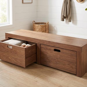 May include: A rectangular wooden storage bench with a warm brown wood grain finish. The bench features two large pull-out drawers with integrated rectangular handle cutouts. One drawer is open, revealing a folded light-colored textile inside.
