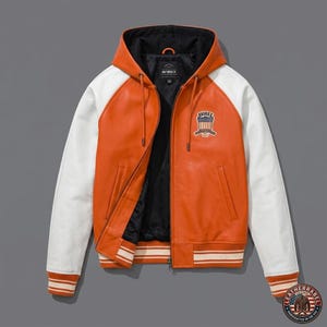 K&ouml;nnte beinhalten: Orange-wei&szlig;e Lederjacke mit Kapuze. Die Jacke hat wei&szlig;e &Auml;rmel, einen orangefarbenen K&ouml;rper und ein schwarzes Innenfutter. Sie hat einen Rei&szlig;verschluss und einen Aufn&auml;her auf der Brust mit der Aufschrift "AVIREX". Die Manschetten und der Saum sind gestreift.