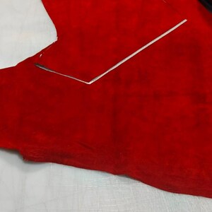 Puede incluir: Una pieza grande de cuero de ante rojo vibrante colocada sobre una superficie de corte blanca. Una regla de metal plateado est&aacute; colocada sobre el material, marcando una l&iacute;nea recta para el corte. Se ven restos de cuero rojo al fondo.