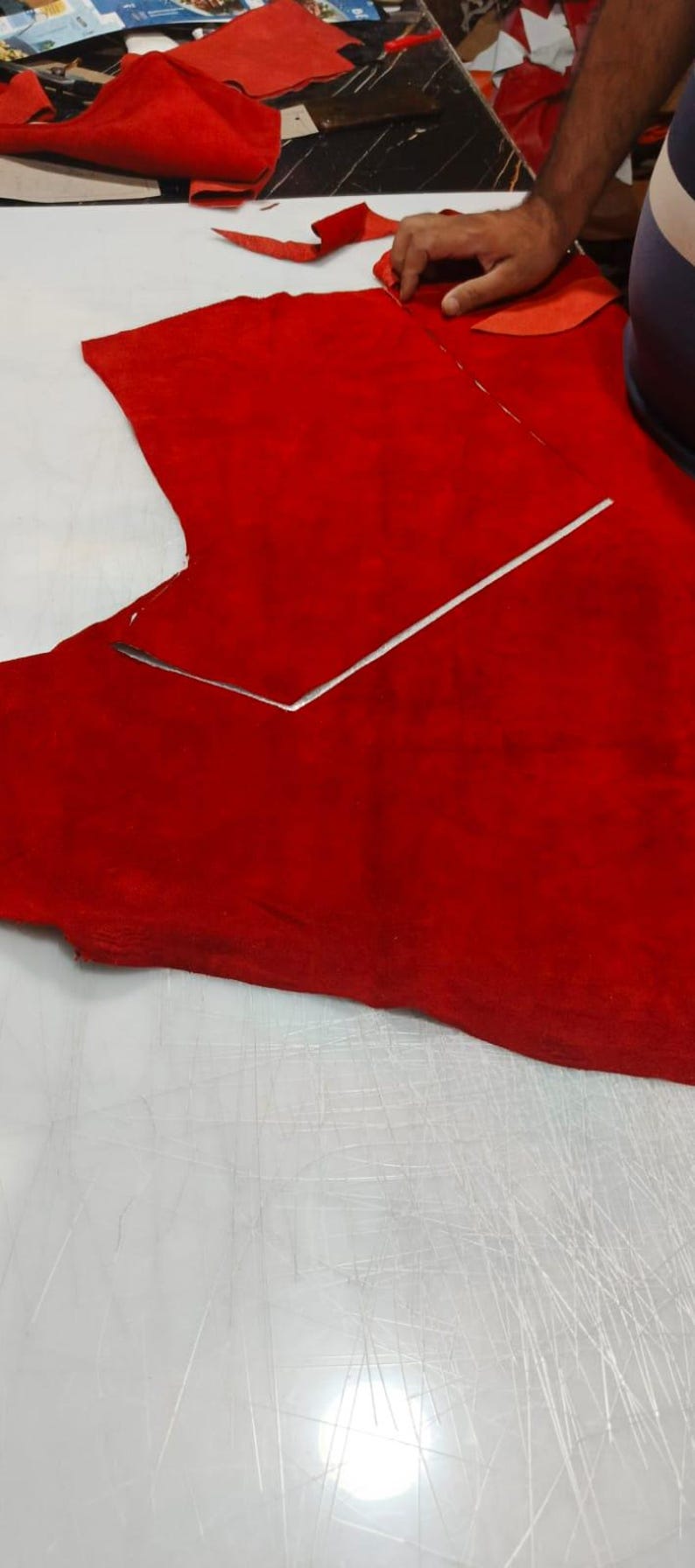 Puede incluir: Una pieza grande de cuero de ante rojo vibrante colocada sobre una superficie de corte blanca. Una regla de metal plateado est&aacute; colocada sobre el material, marcando una l&iacute;nea recta para el corte. Se ven restos de cuero rojo al fondo.