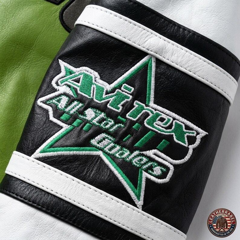 May include: Close-up of a black leather jacket sleeve with white stripes and a green and white embroidered star logo that reads "Avirex All Star Qualers". The jacket has a white and green color scheme.