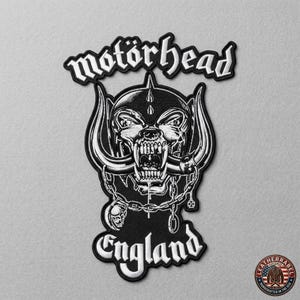 K&ouml;nnte beinhalten: Schwarz-wei&szlig;er, gestickter Aufn&auml;her mit dem Wort "mot&ouml;rhead" &uuml;ber einem Totenkopf-Design. Das Wort "England" steht darunter. Dieser Aufn&auml;her ist zum Aufn&auml;hen auf Kleidung oder Taschen bestimmt.