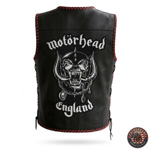 K&ouml;nnte beinhalten: Schwarze Lederweste mit roter geflochtener Bord&uuml;re und seitlichen Schn&uuml;rsenkeln. Die Weste hat eine gro&szlig;e wei&szlig;e Grafik eines Sch&auml;dels mit den Worten "mot&ouml;rhead" und "England" in gotischer Schrift. Die Weste ist handgefertigt in den USA.