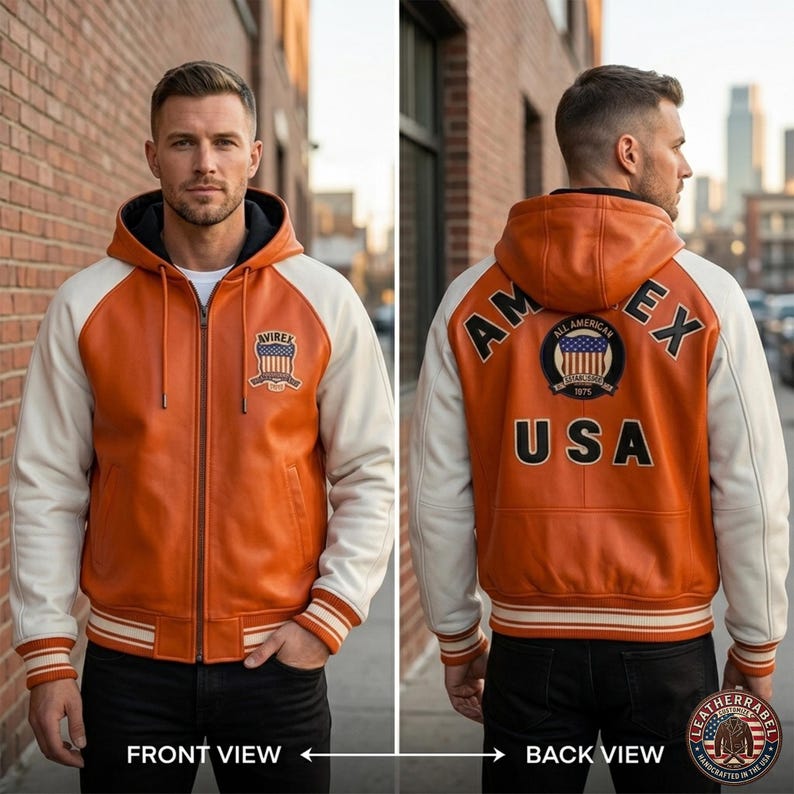 K&ouml;nnte beinhalten: Orange-cremefarbene Lederjacke mit Kapuze. Die Jacke hat einen Frontrei&szlig;verschluss, gerippte B&uuml;ndchen und einen gestreiften Saum. Auf der Vorderseite befindet sich ein Aufn&auml;her mit Text, auf der R&uuml;ckseite "AM EX USA" und ein rundes Emblem.