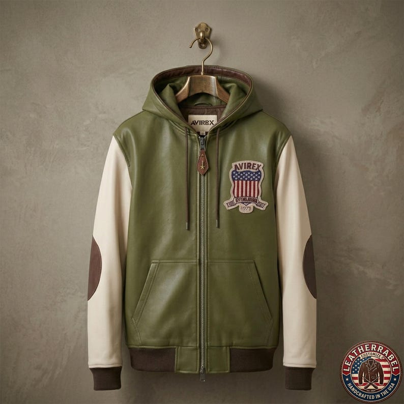 May include: An olive green leather hoodie jacket with cream-colored sleeves and dark brown elbow patches. The jacket features a front zipper, a hood with drawstrings, and a patch on the chest displaying the text AVIREX with a US flag shield design.