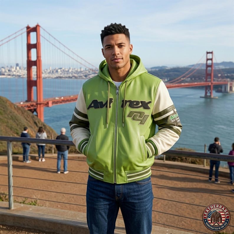May include: A green and cream-colored zip-up jacket with the text "Avirex" on the chest and "R4" on the front. The jacket has a hood and is worn with blue jeans. The Golden Gate Bridge is in the background.