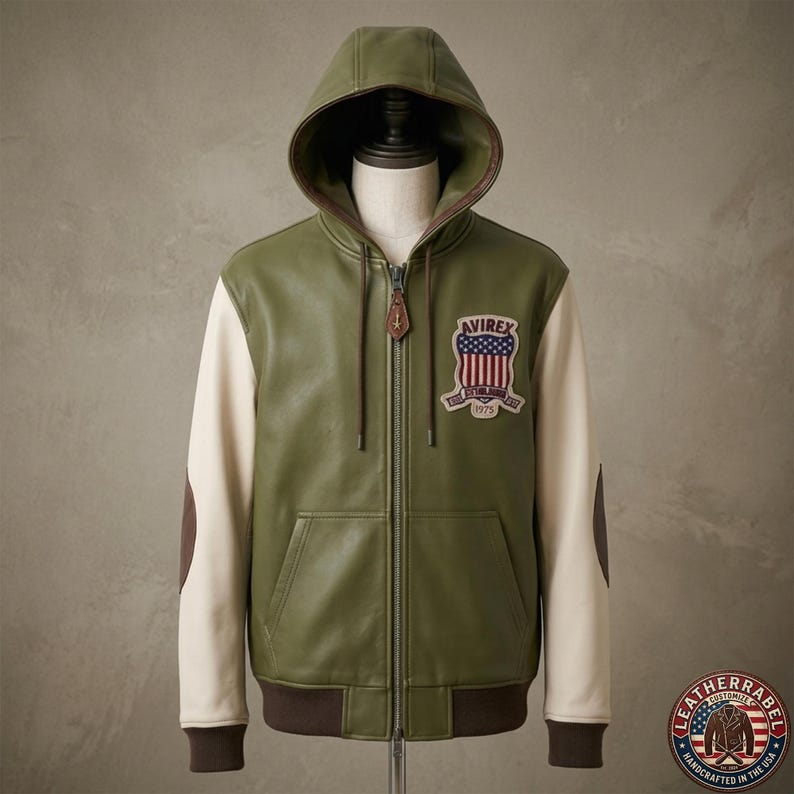 May include: An olive green leather hooded jacket with cream-colored sleeves and brown elbow patches. The front features a full-length zipper with a leather pull tab and an embroidered patch on the chest displaying the text AVIREX and 1975.