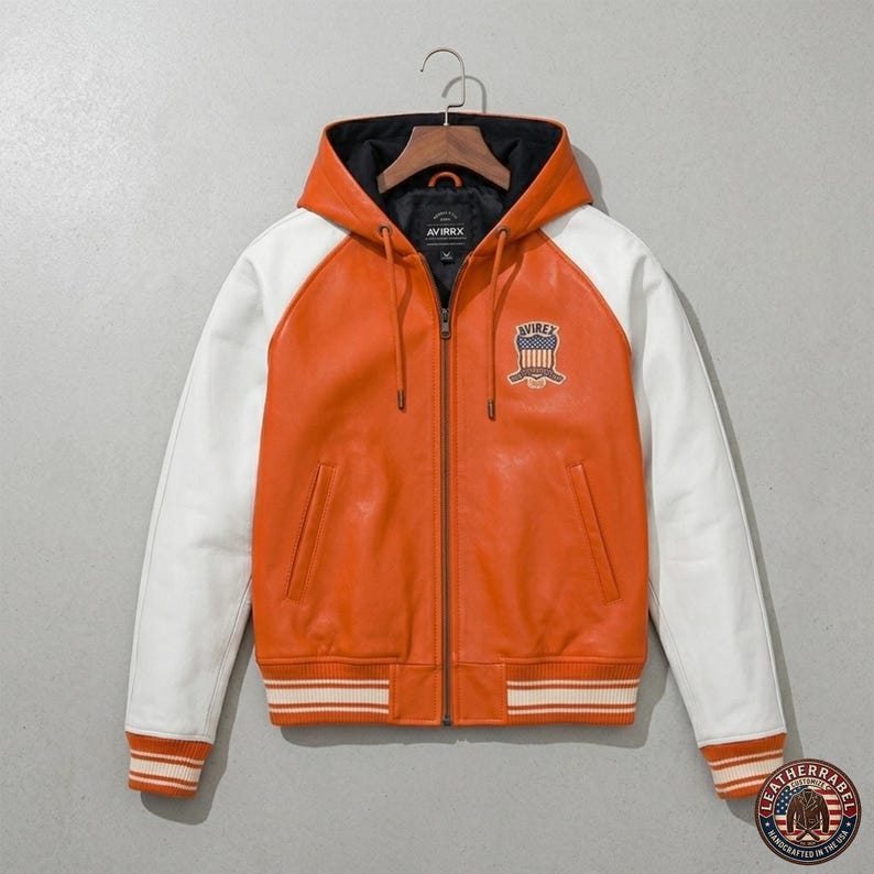 K&ouml;nnte beinhalten: Orange-wei&szlig;e Lederjacke mit Kapuze. Die Jacke hat wei&szlig;e &Auml;rmel, ein schwarzes Innenfutter und einen gerippten Saum mit wei&szlig;en Streifen. Sie hat einen Rei&szlig;verschluss und einen Aufn&auml;her mit dem Wort "AVIREX".