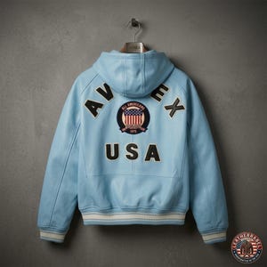 Pu&ograve; includere: Giacca in pelle azzurra con cappuccio, con la scritta "AVIREX USA" sul retro. La giacca presenta una toppa con un disegno della bandiera americana e un bordo a righe bianche e crema sui polsini e sull'orlo.