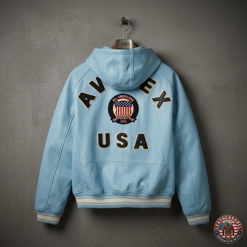 Pu&ograve; includere: Giacca in pelle azzurra con cappuccio, con la scritta "AVIREX USA" sul retro. La giacca presenta una toppa con un disegno della bandiera americana e un bordo a righe bianche e crema sui polsini e sull'orlo.