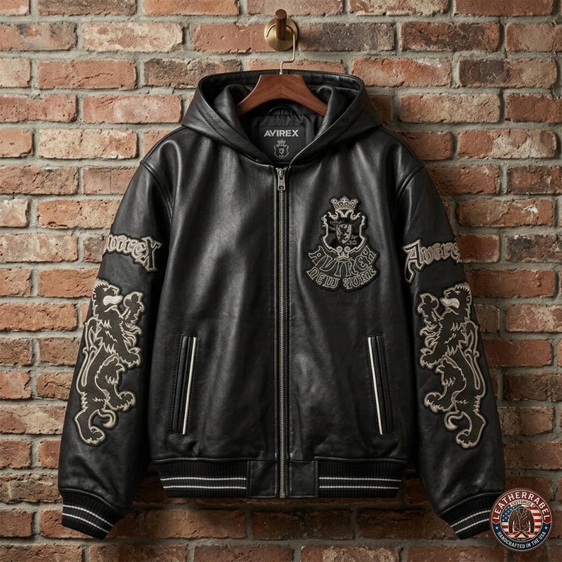 May include: A black leather hooded jacket featuring a full-length front zipper, ribbed cuffs and hem with white stripes, and embroidered patches on the chest and sleeves. The chest patch displays a crest with the text Avirex New York.