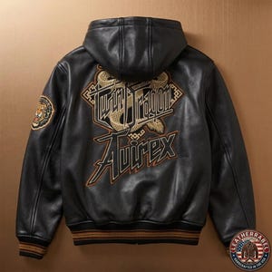 May include: A black leather hooded jacket featuring a large embroidered graphic on the back with the text Twin Dragon and Avirex in gold and black. The sleeves have ribbed cuffs with brown stripes, and a tiger patch is visible on the upper left arm.