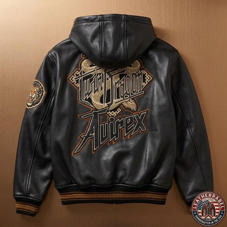 May include: A black leather hooded jacket featuring a large embroidered graphic on the back with the text Twin Dragon and Avirex in gold and black. The sleeves have ribbed cuffs with brown stripes, and a tiger patch is visible on the upper left arm.