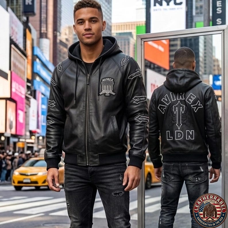 May include: Black leather jacket with a hood, zipper closure, and embroidered details. The jacket features the "AVIREX" logo on the chest and back, with "LDN" below. The model is wearing black jeans in a city setting.