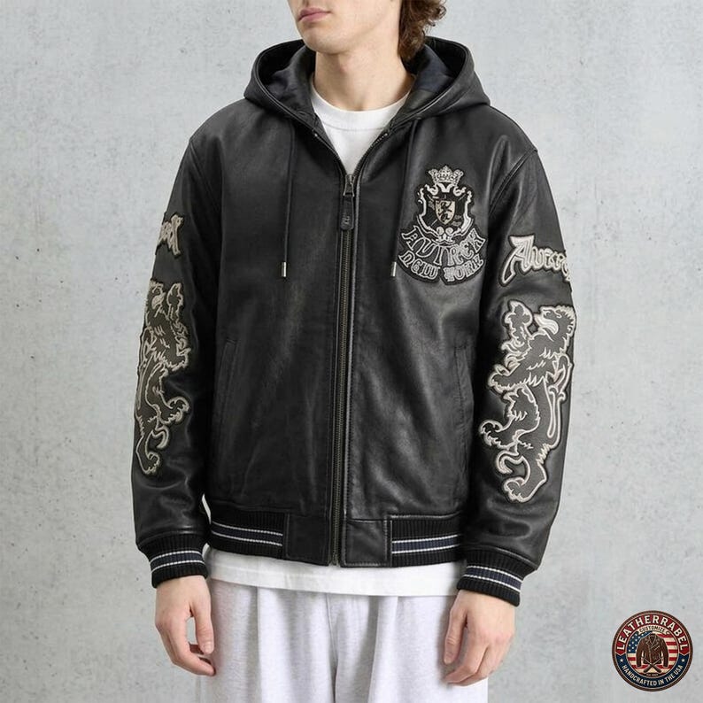May include: A black leather hooded jacket featuring a front zipper closure, ribbed cuffs, and white embroidered crests on the chest and sleeves. The chest emblem displays the text "AUTHOR NEW YORK" with a crown and shield design.