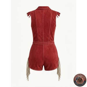 Puede incluir: Un romper de ante rojo sin mangas con cuello, costuras verticales y largos flecos en los hombros y en las aberturas de las piernas. La prenda incluye un logotipo en la esquina inferior derecha con el texto LEATHERLABEL.
