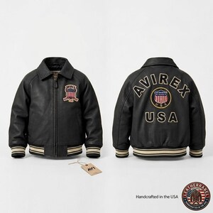 Puede incluir: Chaqueta de cuero negra con un estilo bomber cl&aacute;sico. Cuenta con cuello, cierre de cremallera y pu&ntilde;os y dobladillo acanalados con rayas crema y doradas. La parte delantera tiene un parche y la parte trasera muestra un bordado "AVIREX USA".