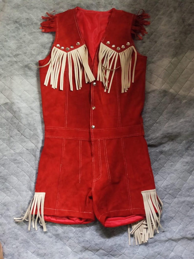 Puede incluir: Un romper rojo brillante sin mangas con detalles de flecos color crema en los hombros y en las aberturas de las piernas. La prenda incluye botones de presi&oacute;n de metal plateado en la parte delantera y un forro interior rojo a juego.