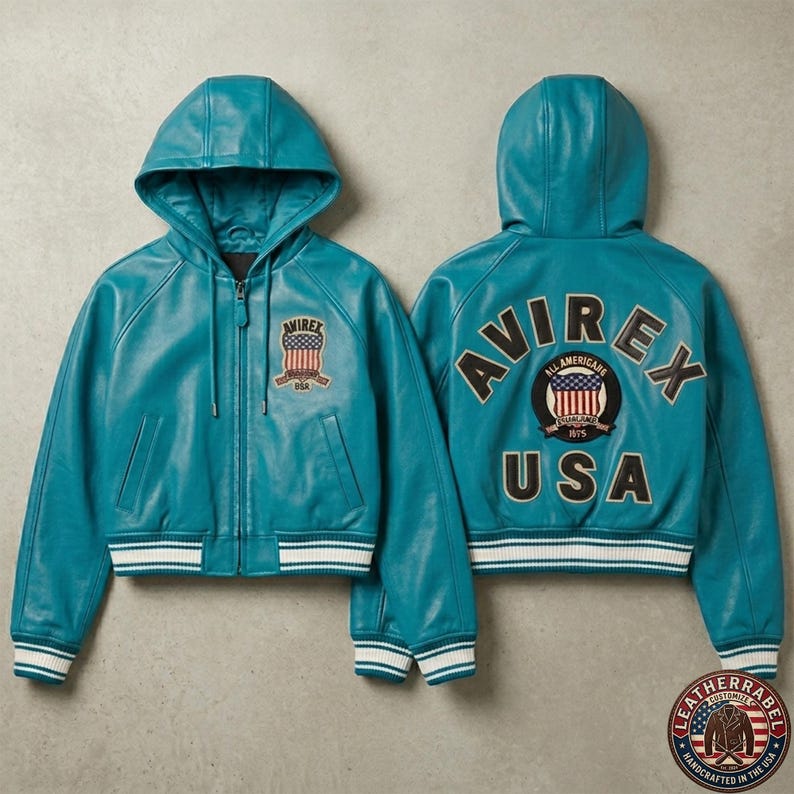 K&ouml;nnte beinhalten: Eine t&uuml;rkisfarbene Lederjacke mit Kapuze und Rei&szlig;verschluss, die auf der Brust einen kleinen Aufn&auml;her mit einer amerikanischen Flagge und dem Text AVIREX tr&auml;gt. Der R&uuml;cken zeigt den Schriftzug AVIREX USA und ein rundes Abzeichen.