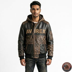 May include: A brown and black leather jacket with a hood. The jacket features the word "AVIREX" across the chest. The jacket has a bomber style with ribbed cuffs and hem. The jacket is worn with blue jeans.