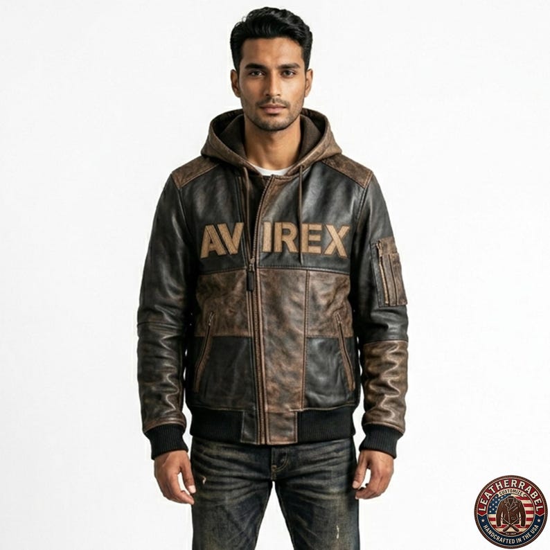 May include: A brown and black leather jacket with a hood. The jacket features the word "AVIREX" across the chest. The jacket has a bomber style with ribbed cuffs and hem. The jacket is worn with blue jeans.