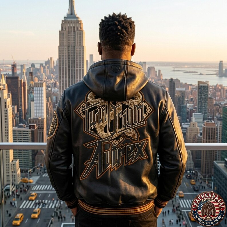 May include: A black leather hooded jacket featuring a large embroidered graphic on the back with the text Twin Dragon and Avirex in gold and brown thread. The jacket has ribbed cuffs and a hem with brown stripes, showcasing detailed stitching.