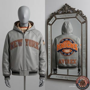 Puede incluir: Una chaqueta de cuero gris con capucha que presenta el texto NEW YORK en letras naranjas y azules en el pecho. La parte posterior, reflejada en un espejo, muestra un gran logotipo circular KNICKS KITH YORK en naranja y azul, con texto AVIREX.