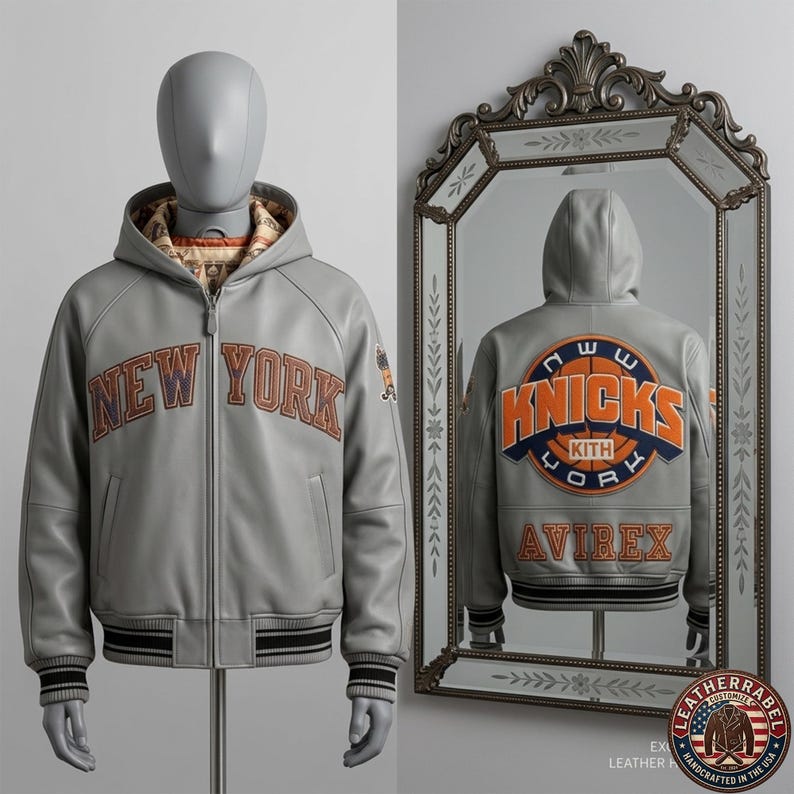 Puede incluir: Una chaqueta de cuero gris con capucha que presenta el texto NEW YORK en letras naranjas y azules en el pecho. La parte posterior, reflejada en un espejo, muestra un gran logotipo circular KNICKS KITH YORK en naranja y azul, con texto AVIREX.