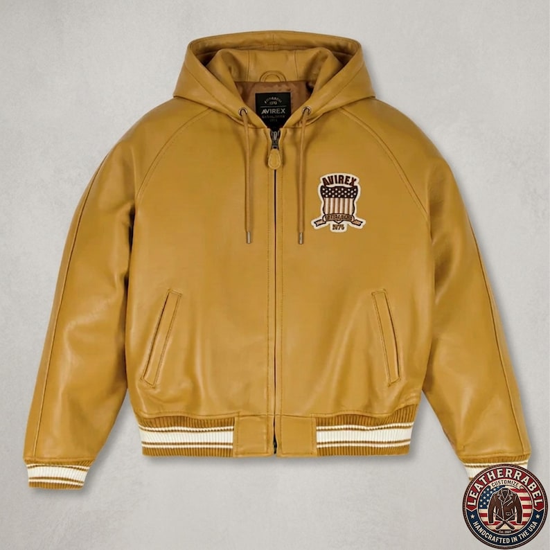 May include: Mustard yellow leather hooded jacket with a zip-up front, featuring a white and cream striped hem and cuffs. The jacket has a patch on the chest with the text "AVIREX" and "1975". A leather label is visible at the bottom right.
